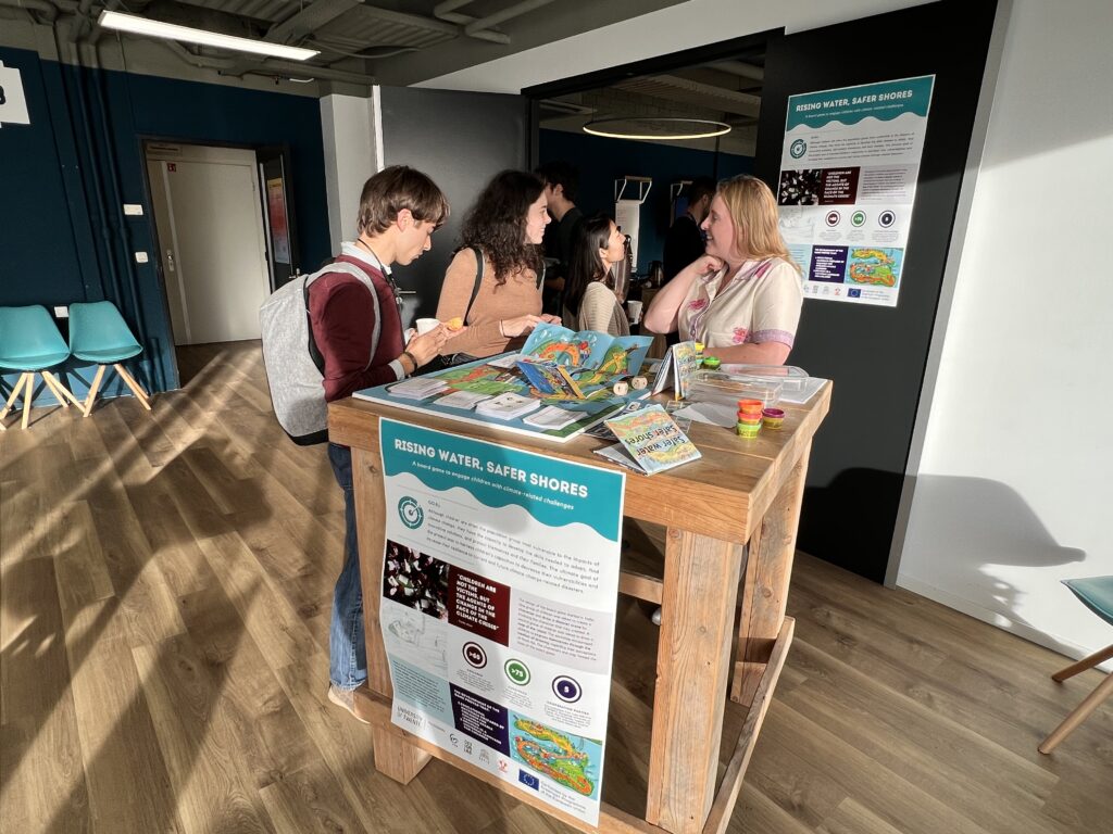 People at an exhibition talking and looking at a board game. Two posters read "Rising Water, Safer Shores"